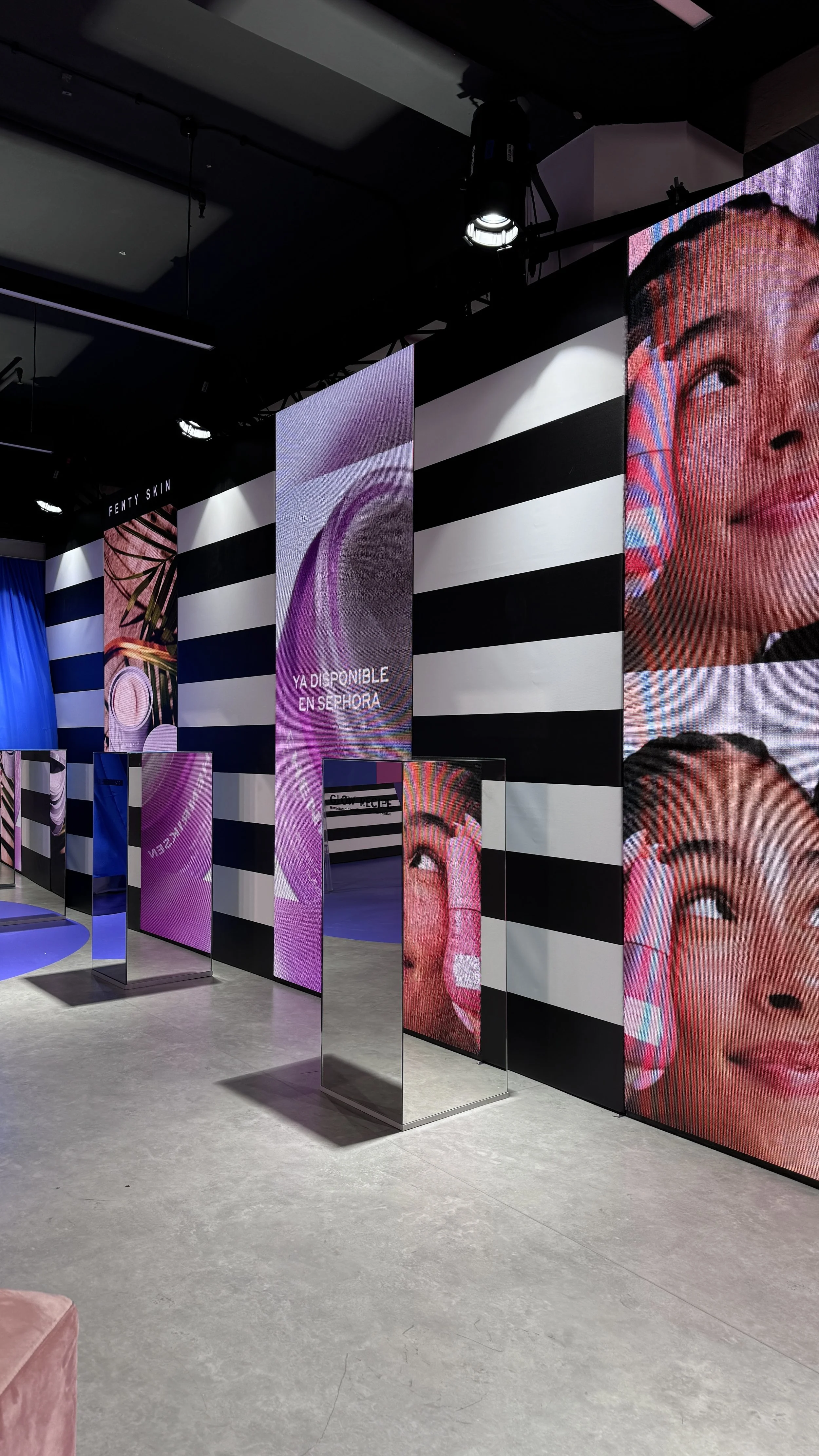 Interior of a retail space with digital displays showcasing Fenty Skin products, black and white striped walls, and a grey floor.