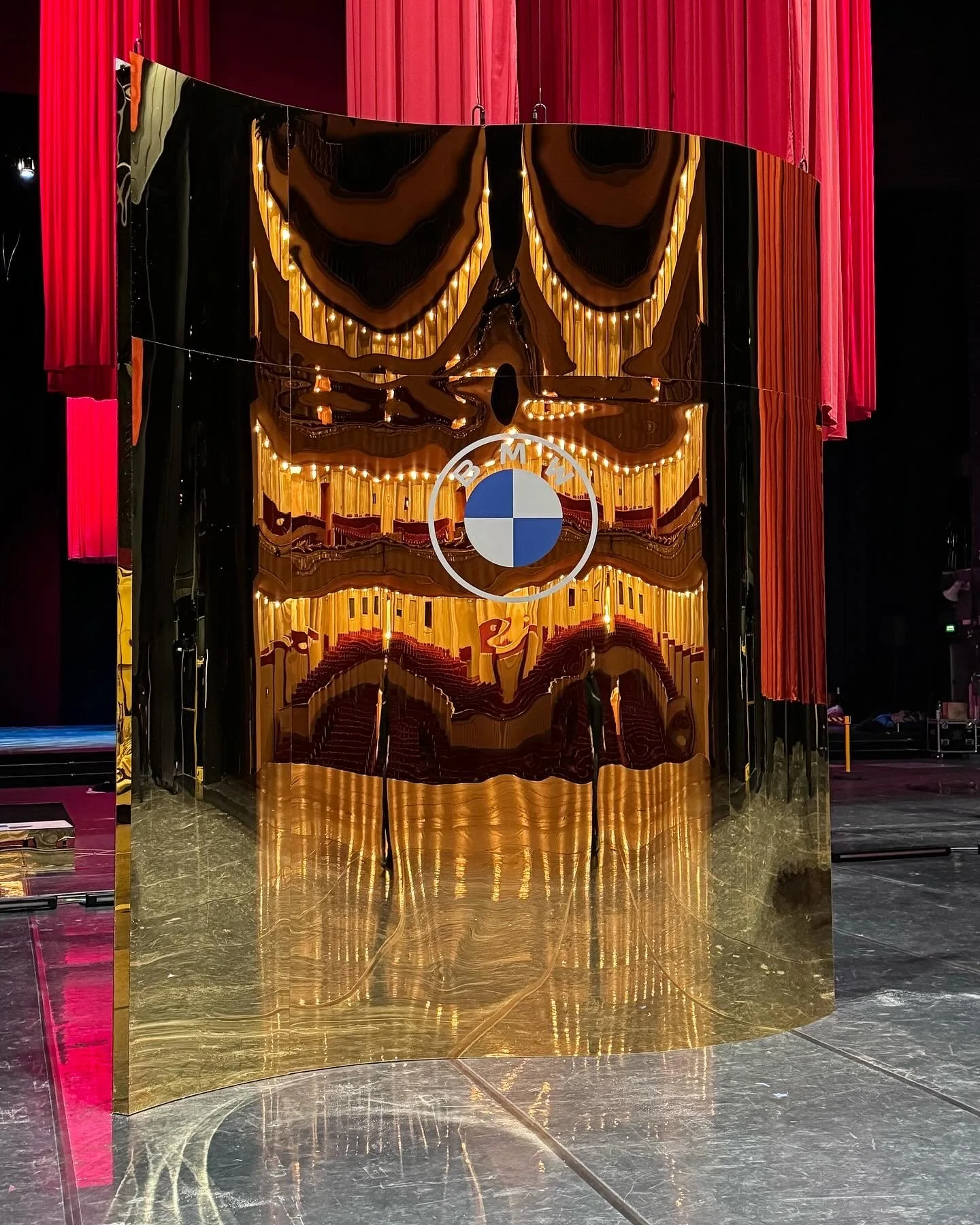 A shiny, gold-colored reflective wall with the BMW logo on it, surrounded by red curtains.