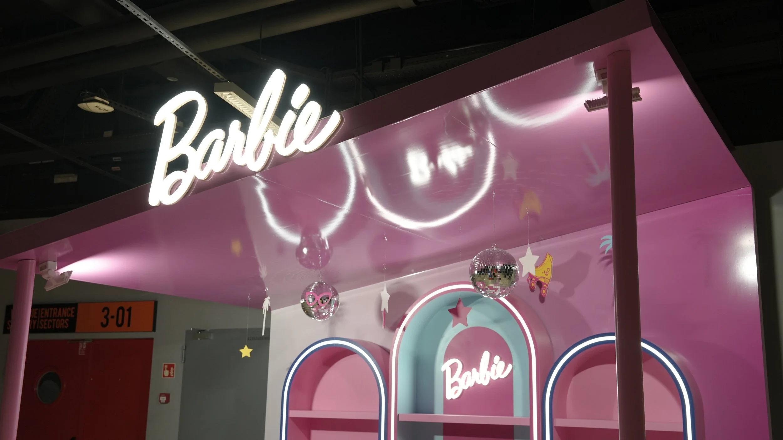 Pink Barbie-themed display area with illuminated Barbie logo, hanging disco balls, and decorative stars and accessories.