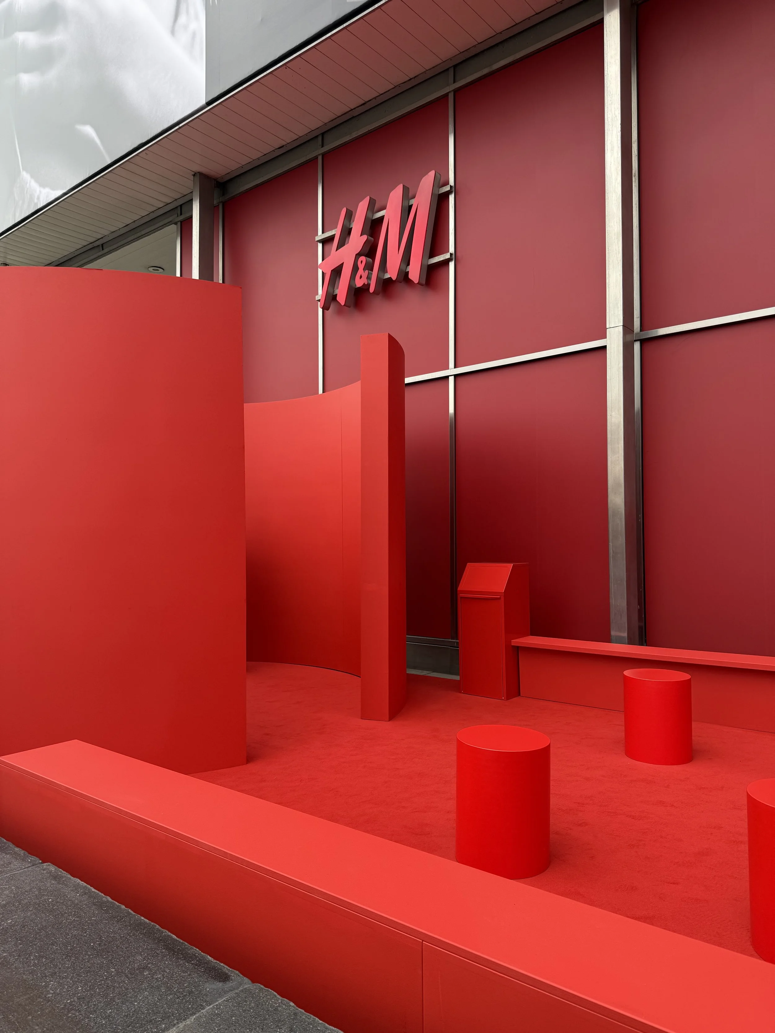 Red display at an H&M store with the logo on a red background, featuring red sculptures and structures on the storefront.