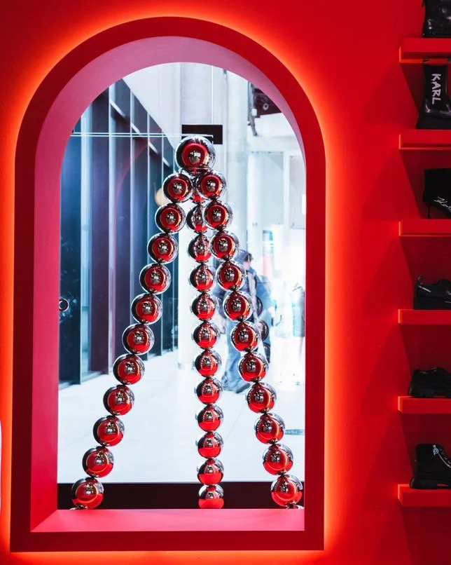 Sculpture of the Christmas tree made with stacked mirrored red spheres within a pink arched frame, standing against a glass window in a retail store.