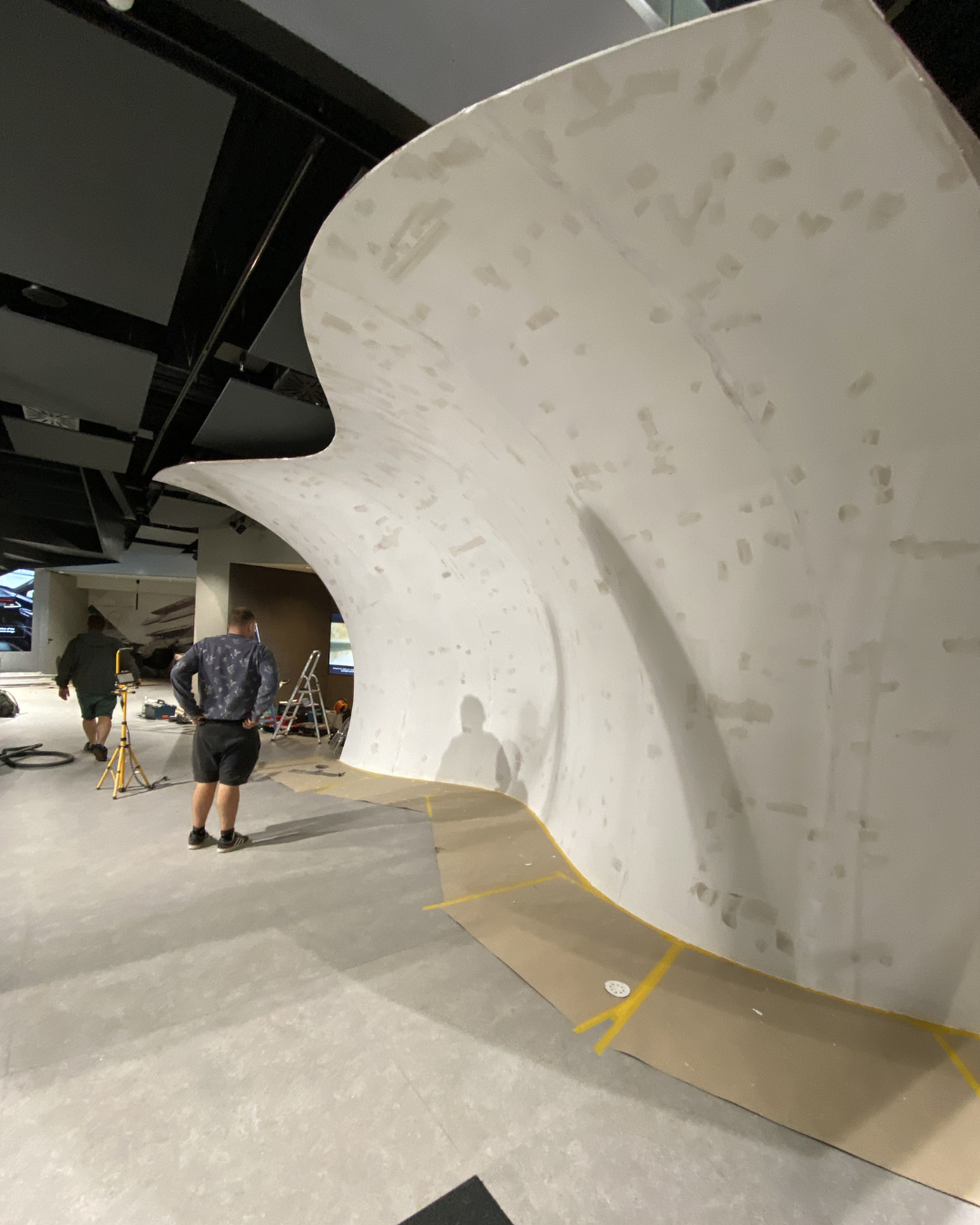 Construction workers installing a large, curved white wall inside a building.