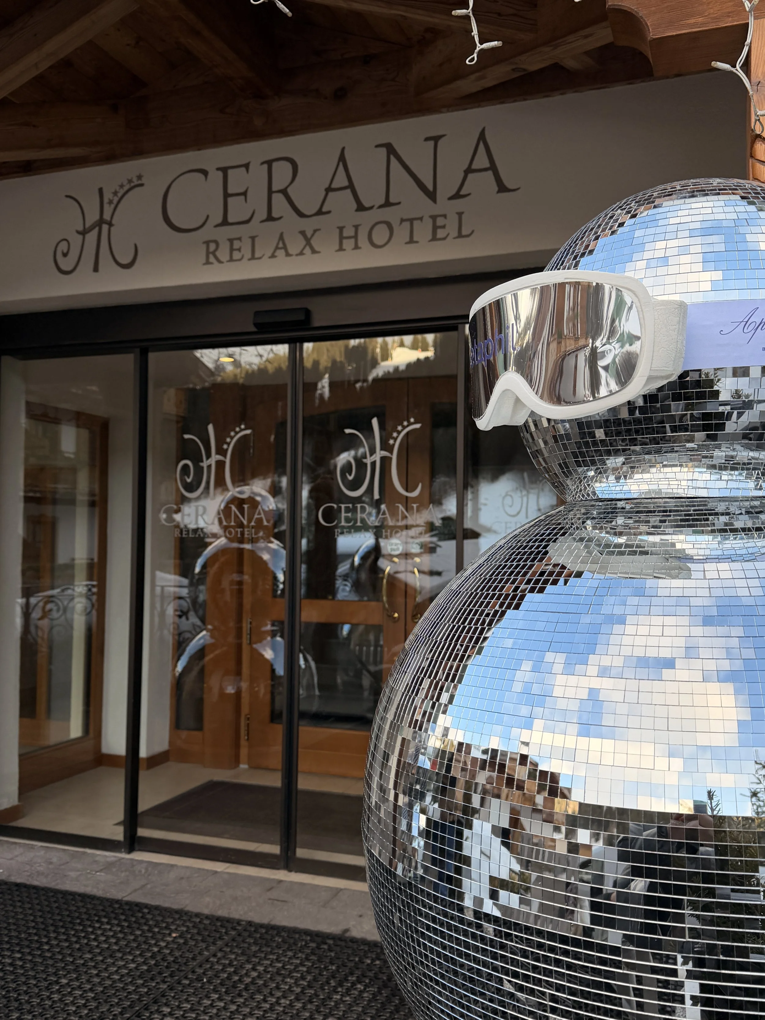 Decorative disco ball sculpture with mirrored tiles and ski goggles resting on it, outside the Cerana Relax Hotel entrance.