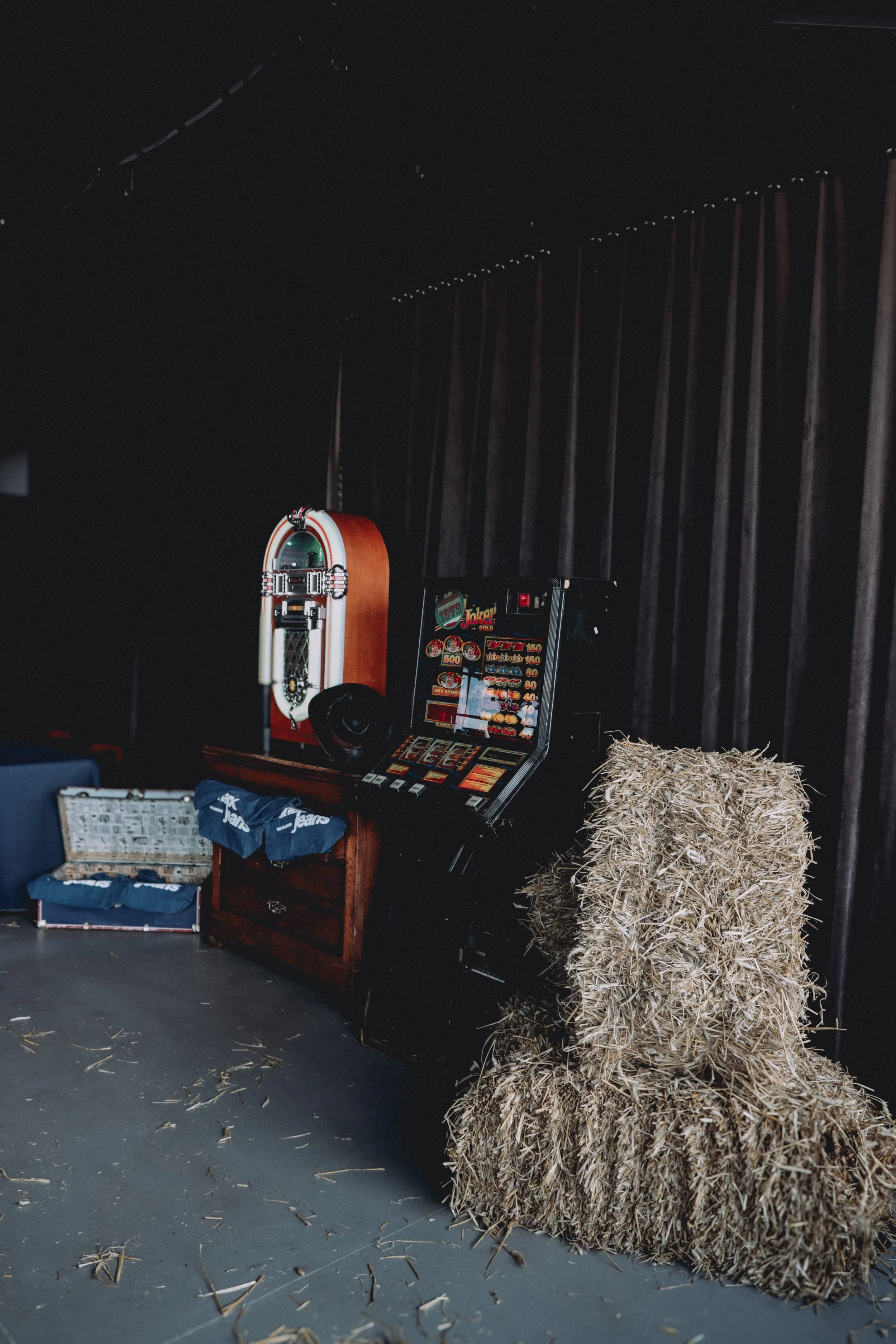 A ball of hay sits on the floor next to a slot machine in a dark room with black walls and string lights overhead.