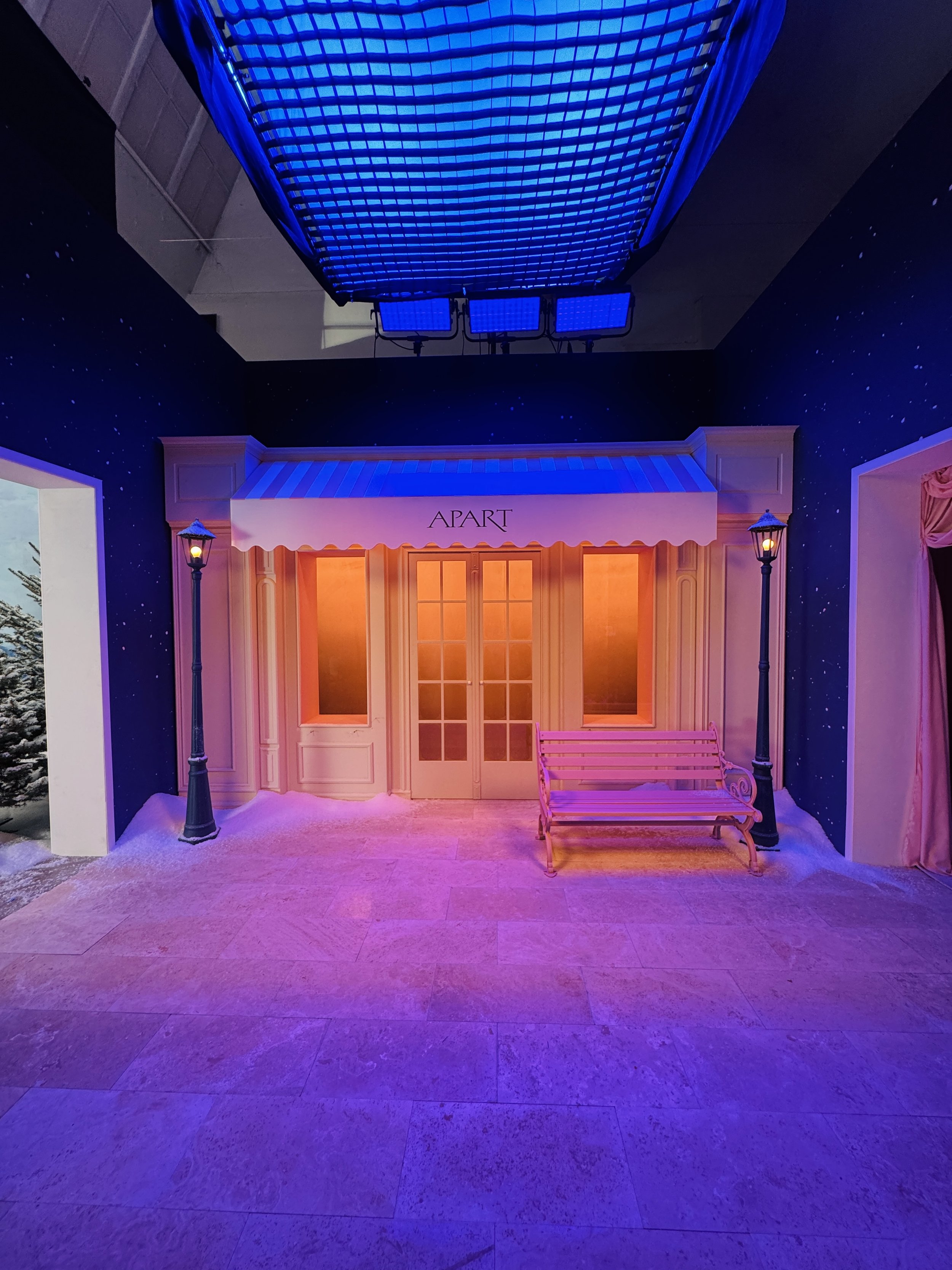 Indoor scene with storefront labeled 'APART' under blue lighting, two street lamps, a pink bench, and snow-covered ground.