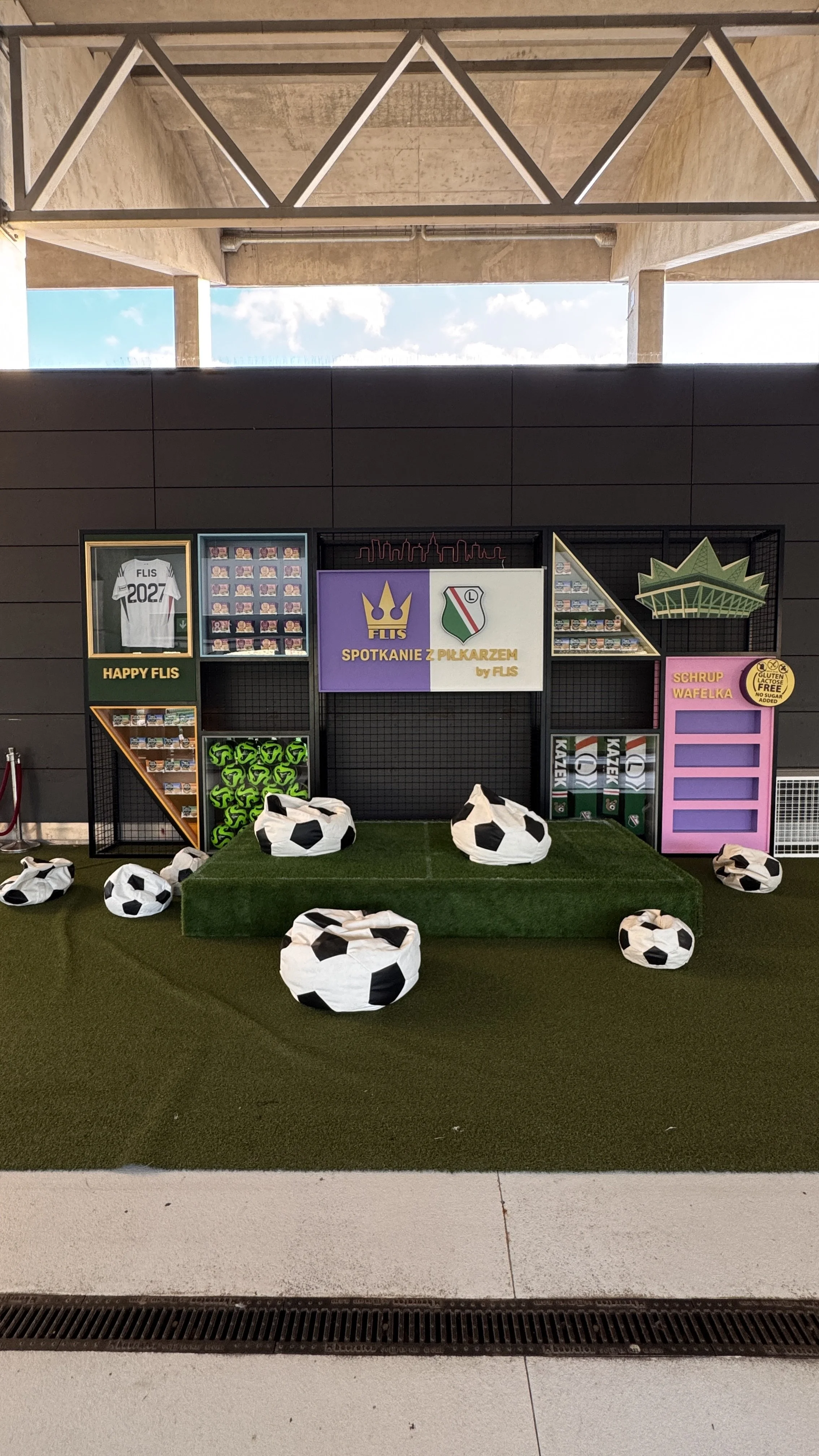 Display setup with soccer-themed items including plush soccer ball seats, a shelf with sports memorabilia, and a central sign in Polish that says 'Waiting Room with Players' surrounded by soccer-themed decorations.