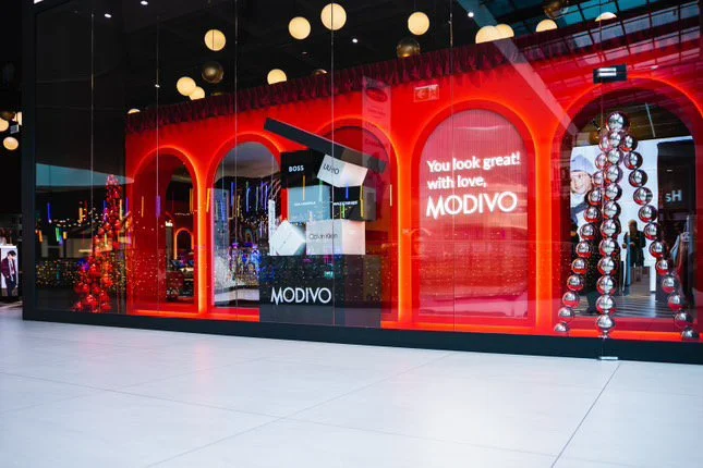 Storefront with large red arches, holiday decorations, and a sign that reads "You look great! with love, MODIVO."