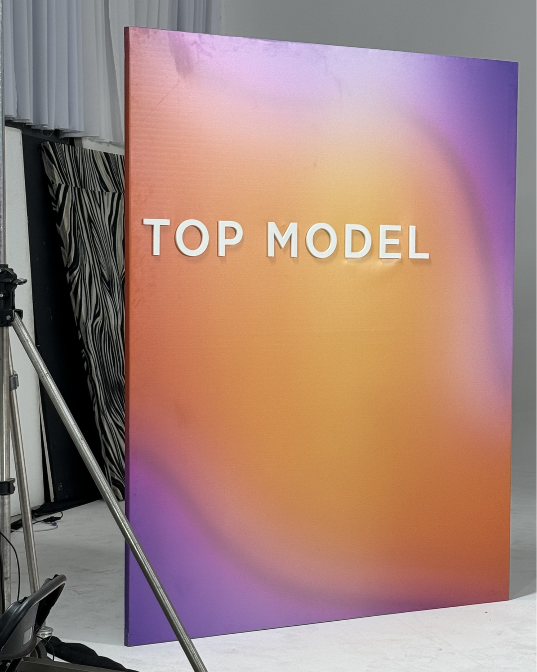 A large, colorful display board with a gradient of purple, pink, and orange tones, featuring the text 'TOP MODEL' in white, raised letters.