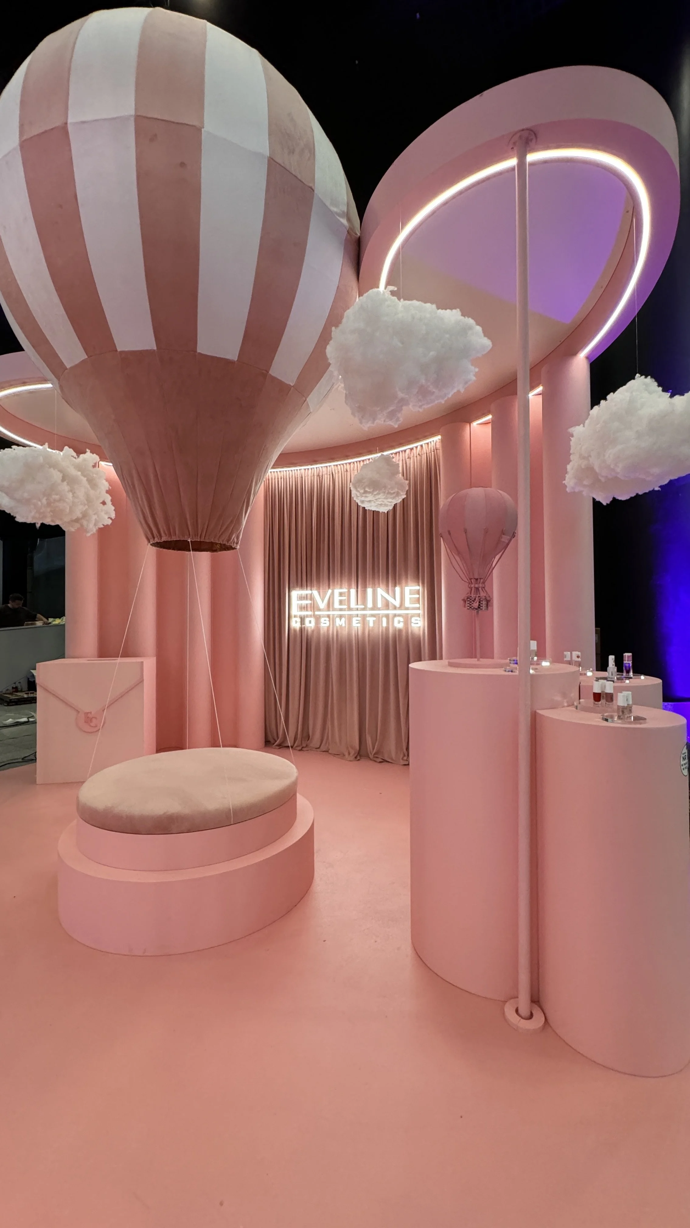 Pink display area with hot air balloon and cloud decorations, illuminated sign reads "Eveline Cosmetics".