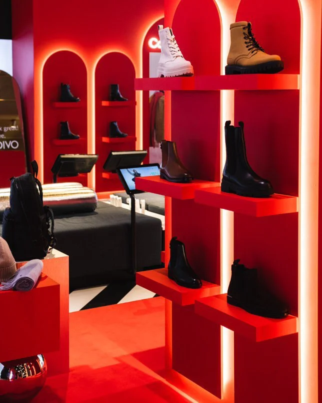 Display of various boots on red shelves in a shoe store with modern lighting and backlit arches.