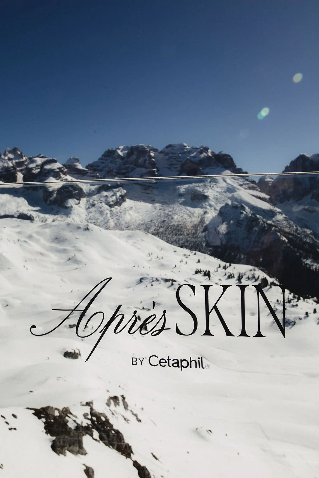 Snow-covered mountain landscape under a clear blue sky with the text 'Apres SKIN BY Cetaphil' at the bottom.