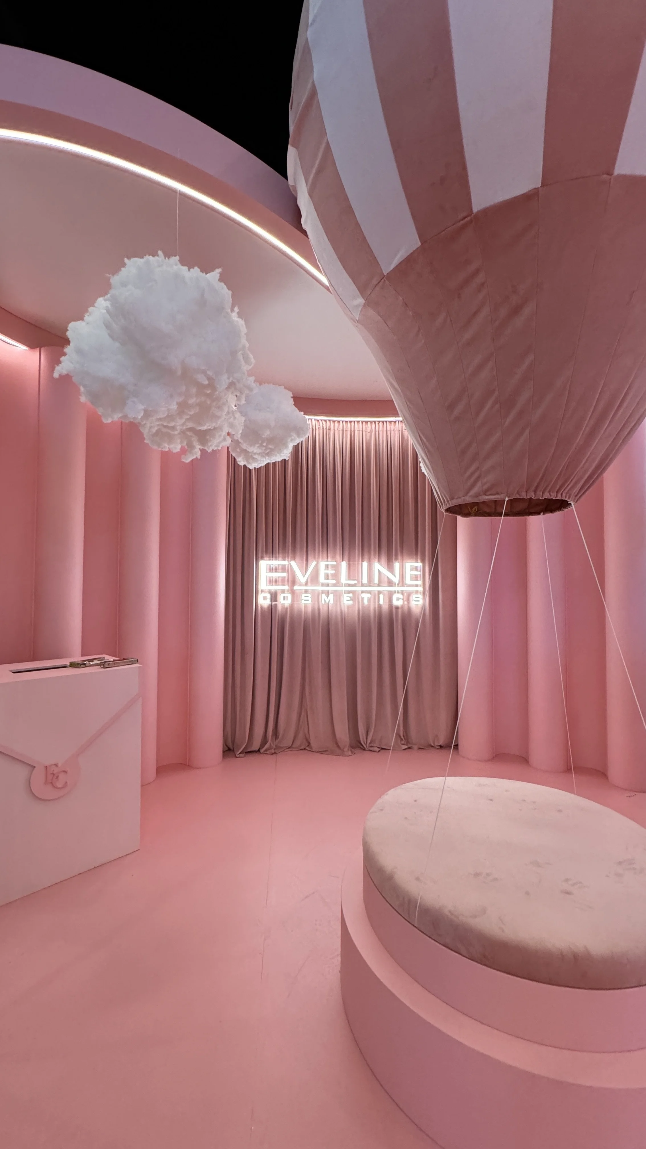 Pink interior of Eylene Cosmetics store with hot air balloon decoration, cloud-shaped hanging decor, and illuminated sign reading "EVELINE COSMETICS".