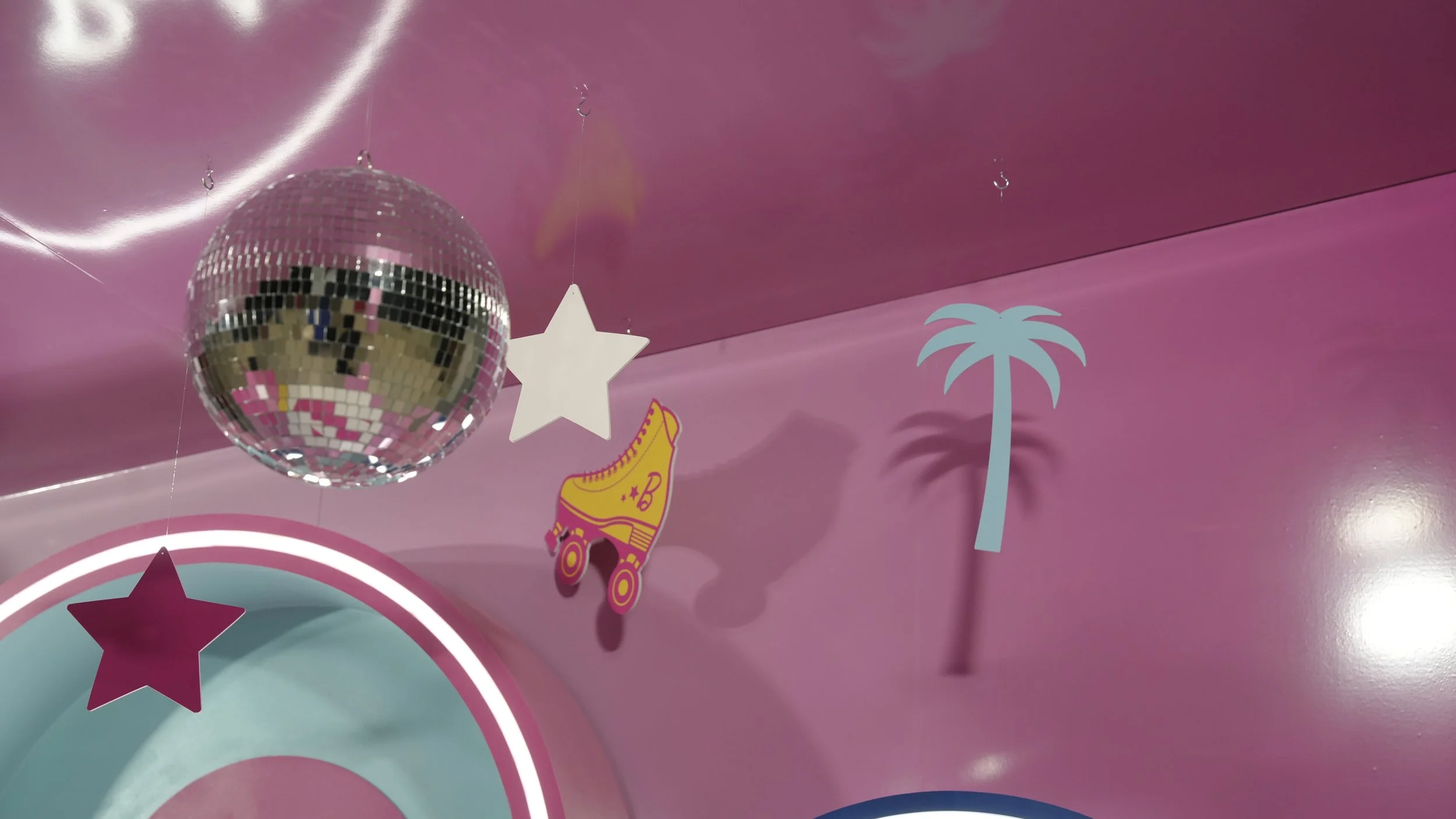Pink ceiling decorated with a mirrored disco ball, a white star ornament, a pink shoe illustration, a palm tree cutout, and a pink star on a circular background.