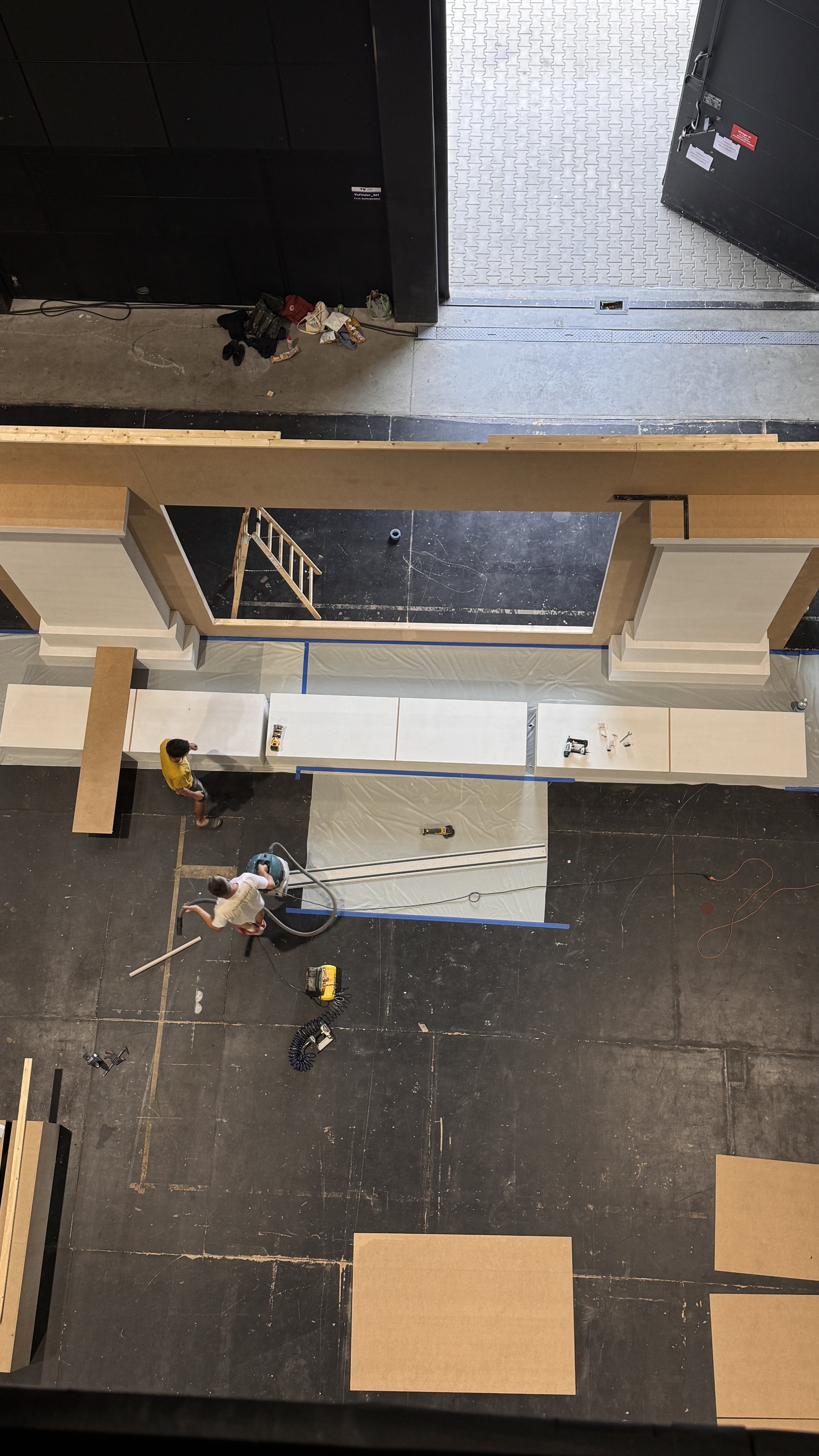 People constructing or renovating a large indoor space, working with tools and materials, with some furniture or fixtures being assembled or installed.