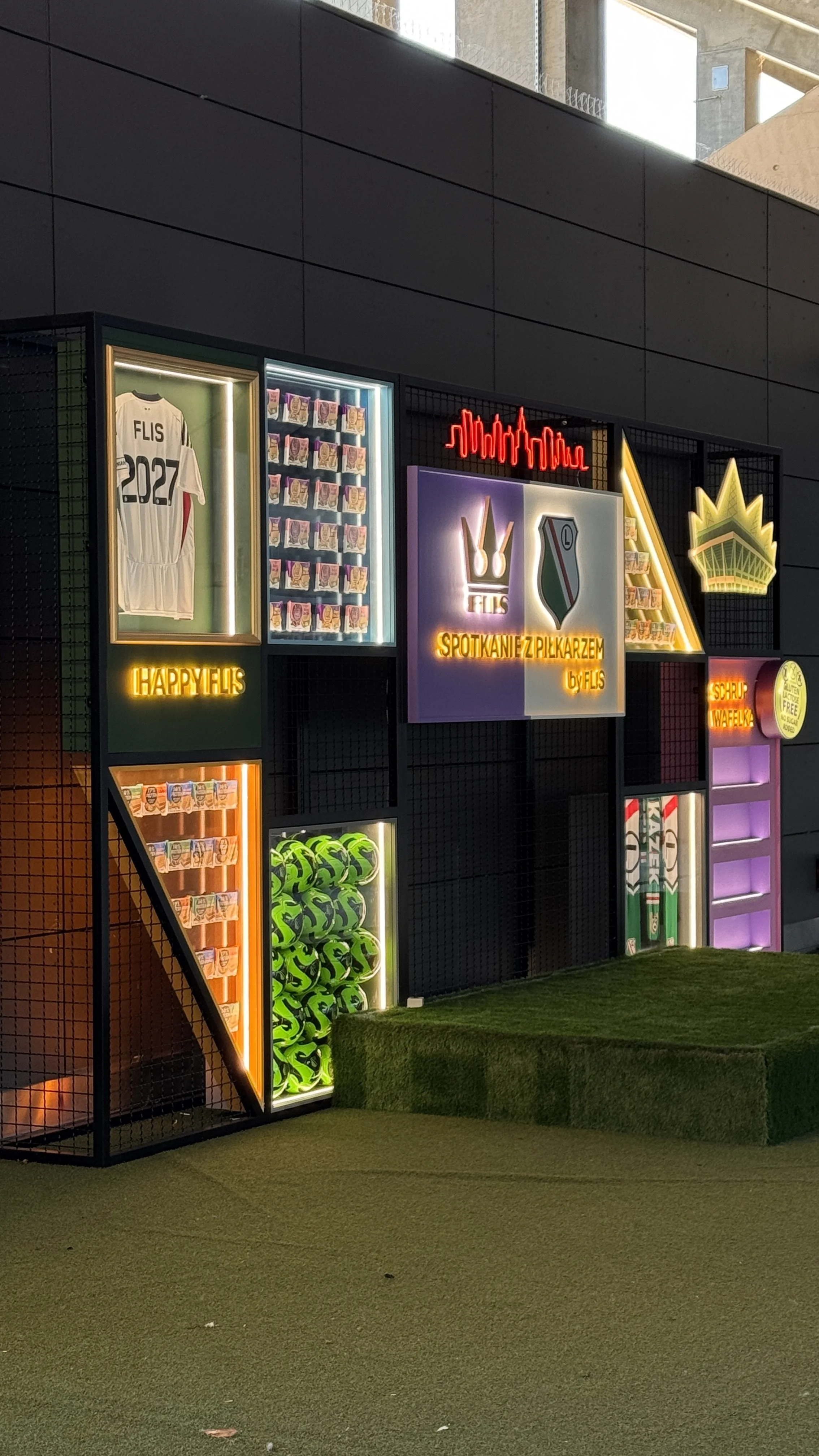 Decorative display with neon and illuminated signs, sports memorabilia, and promotional items on a black metal grid.