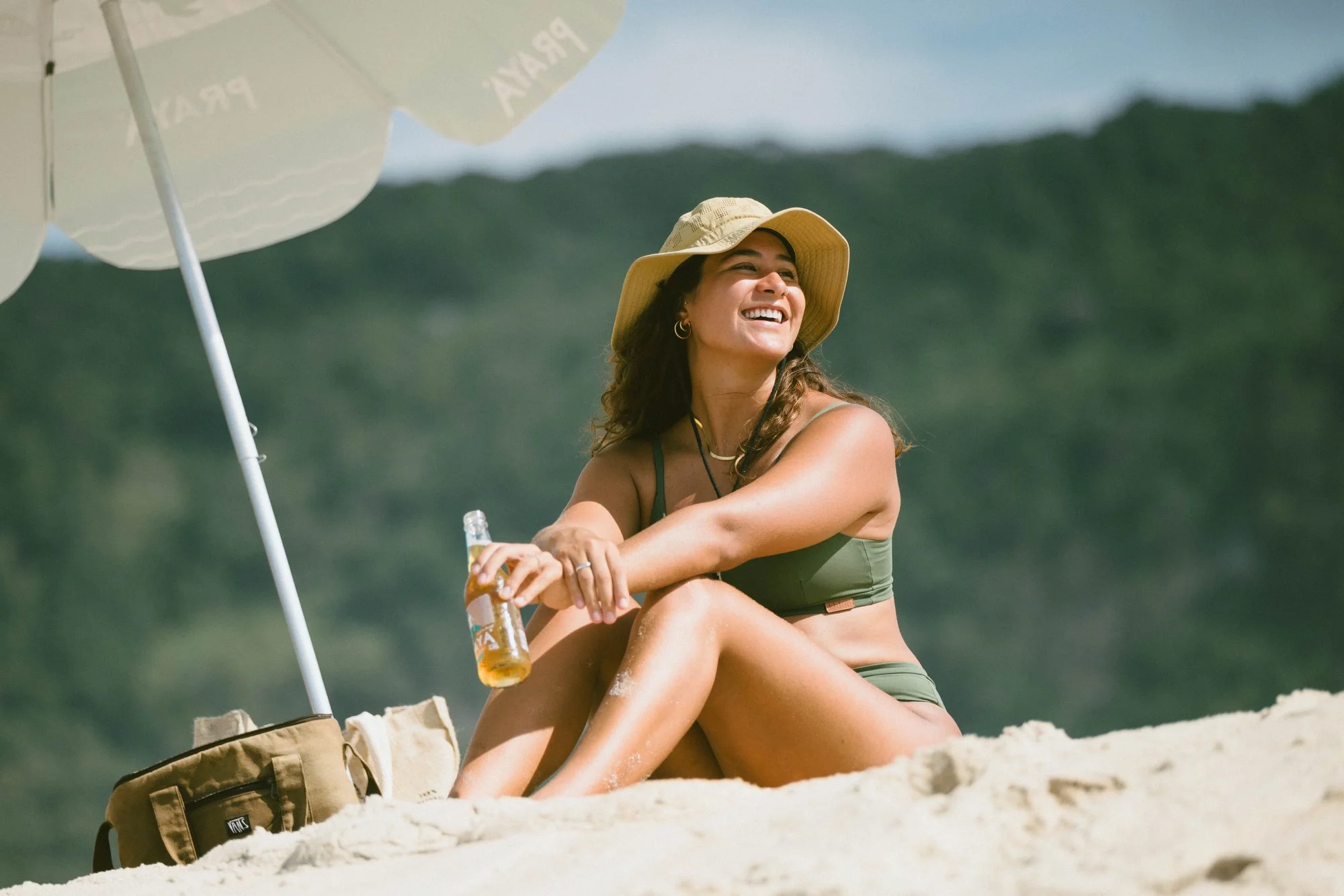 jasmim avelino sentada na areia com cerveja praya na mão