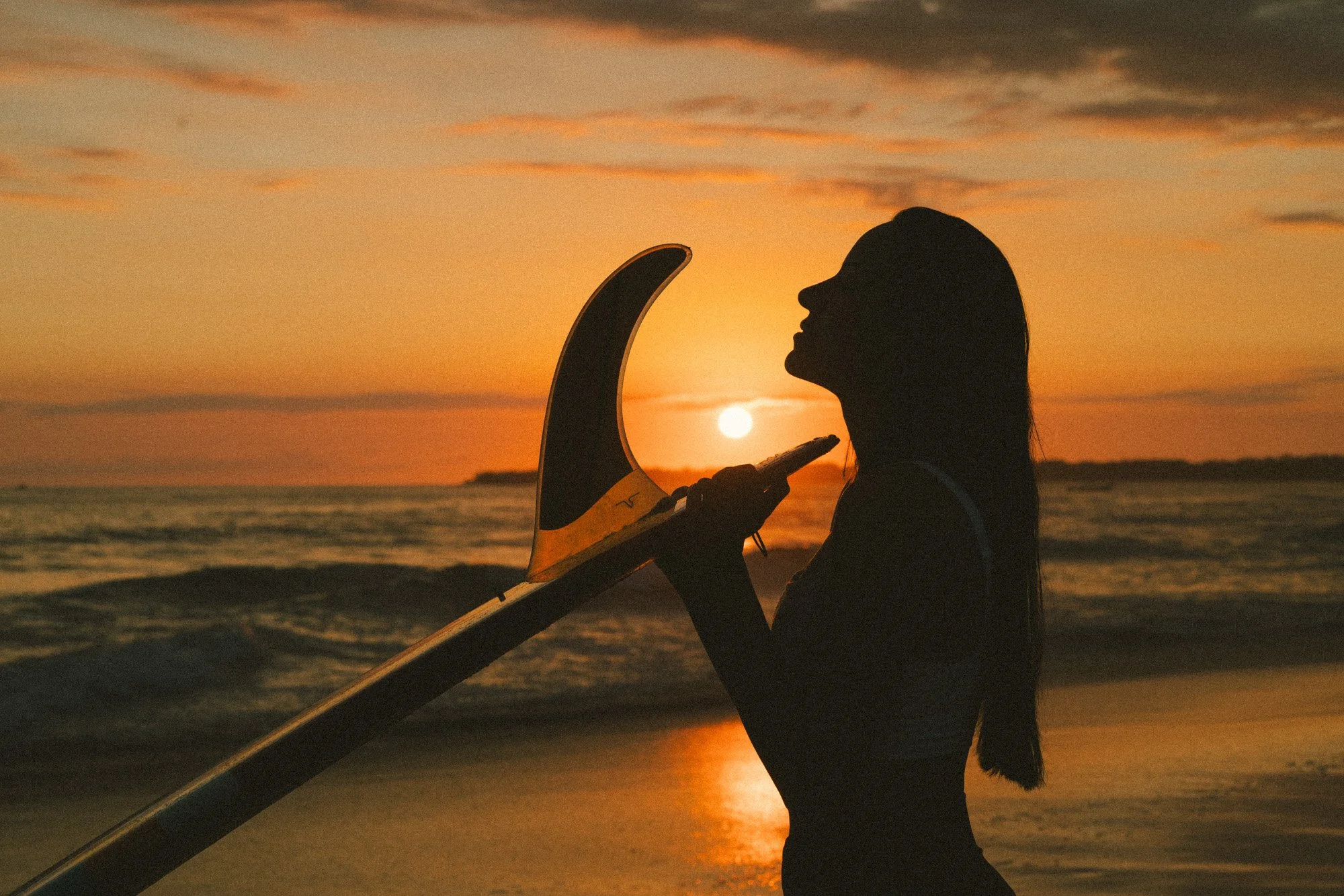 mulher com prancha na luz dourada do por do sol