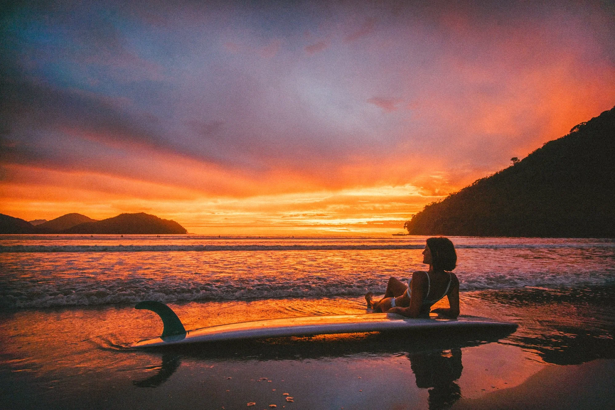 mari marcelli contemplando o nascer do sol com sua prancha no perequê açu em ubatuba