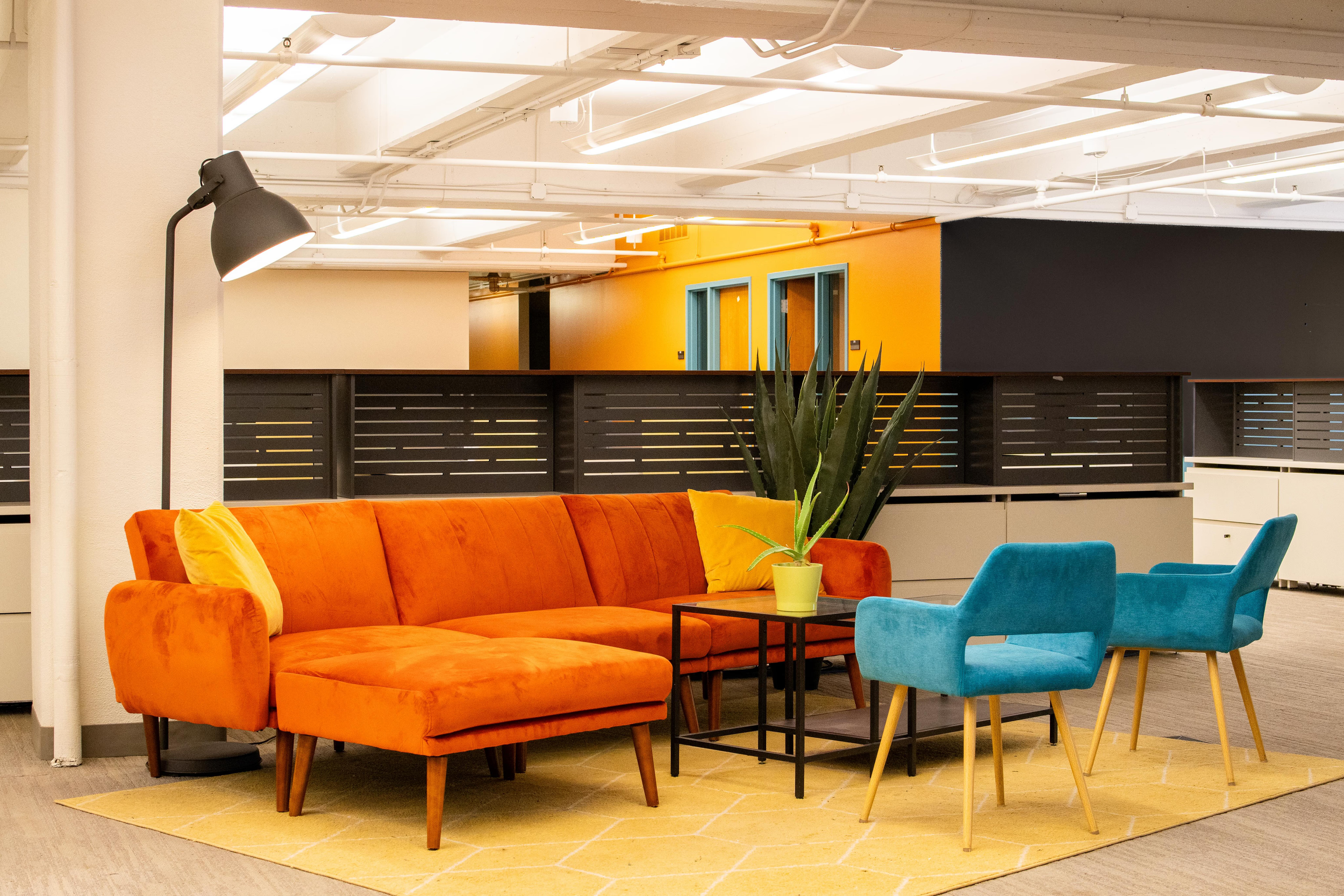 meeting space area with orange couch, blue chair, yellow pillows