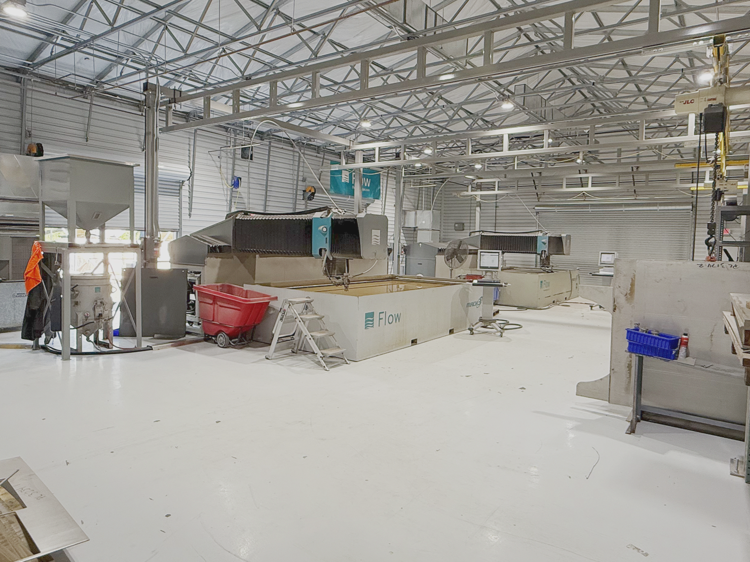Inside a manufacturing facility with large industrial machinery for processing or cutting materials. Bright lighting and a high metal roof are visible.