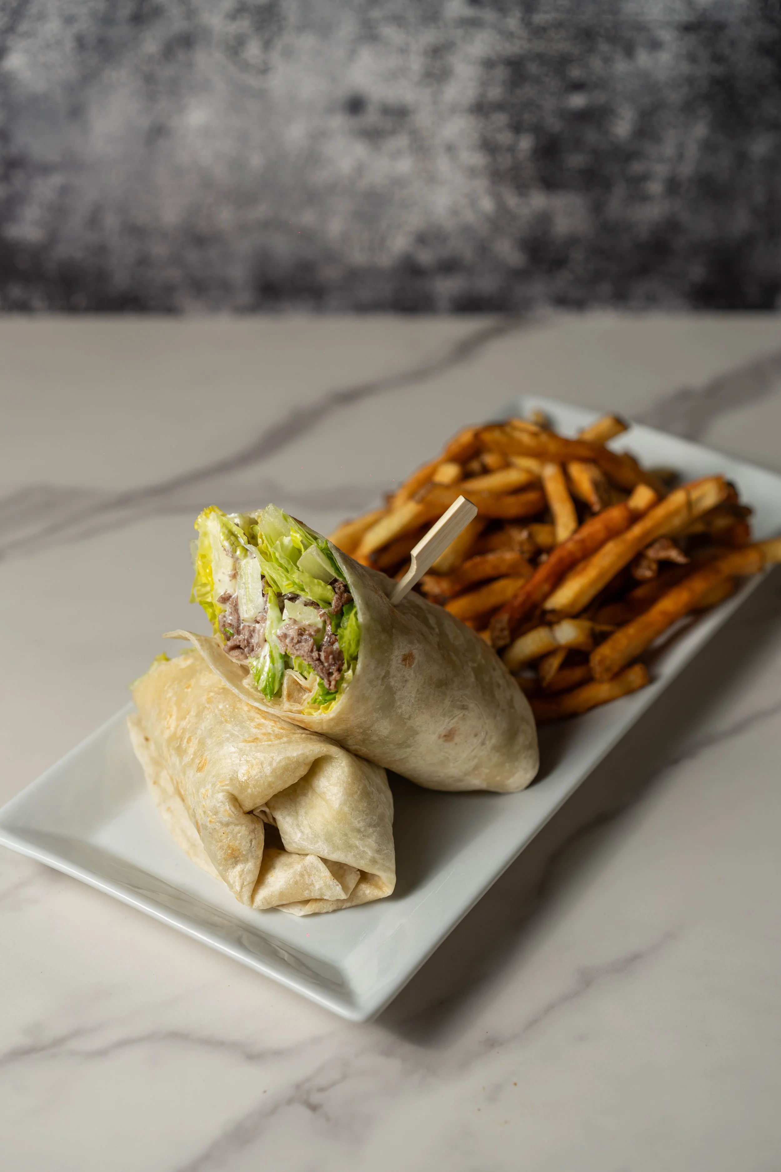 A white rectangular plate with a wrap and a serving of French fries on a marble surface.