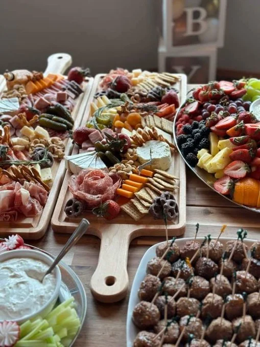 A large assortment of fruits, cheeses, nuts, meats, and snacks arranged on wooden and ceramic platters for a party or gathering.