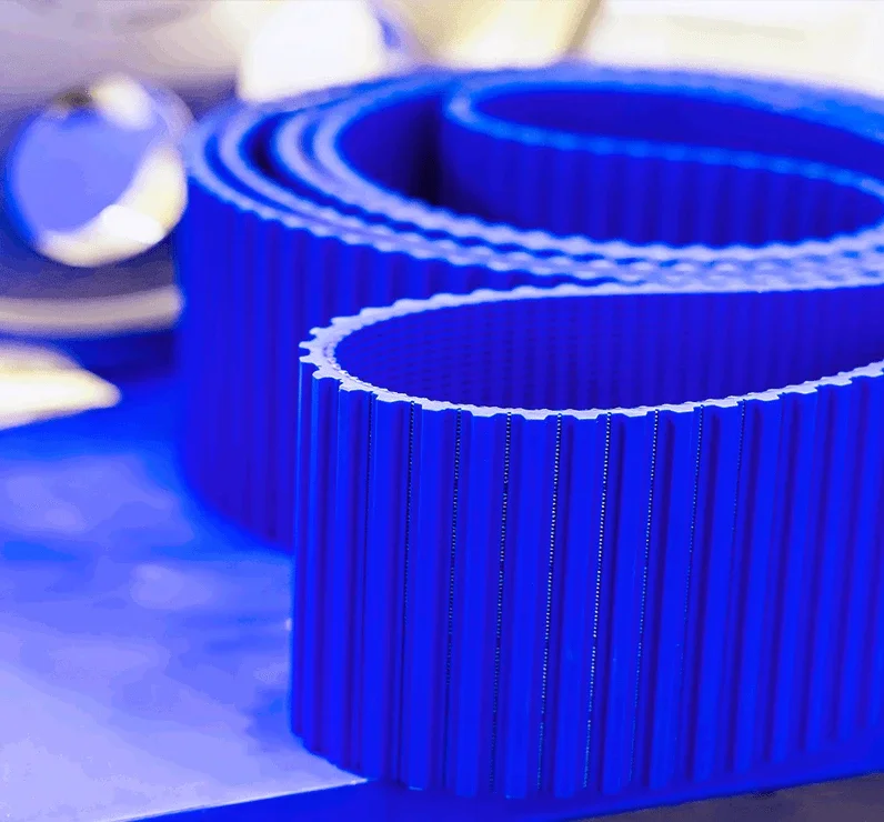 A close-up of a blue industrial timing belt with evenly spaced teeth, coiled on a workbench.
