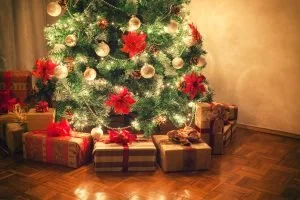Decorated Christmas tree surrounded by wrapped presents on a wooden floor.