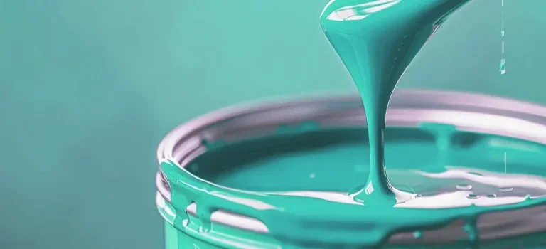 A close-up of a metal container filled with teal-colored paint, with paint being poured into it.
