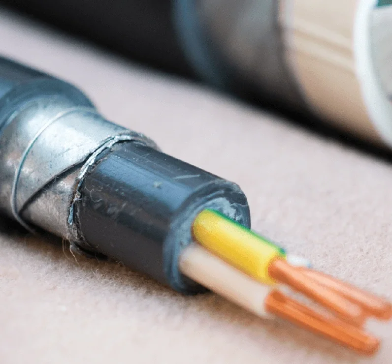 Close-up of a black and silver electrical cable with exposed copper wires and colored insulation, resting on a light-colored surface.