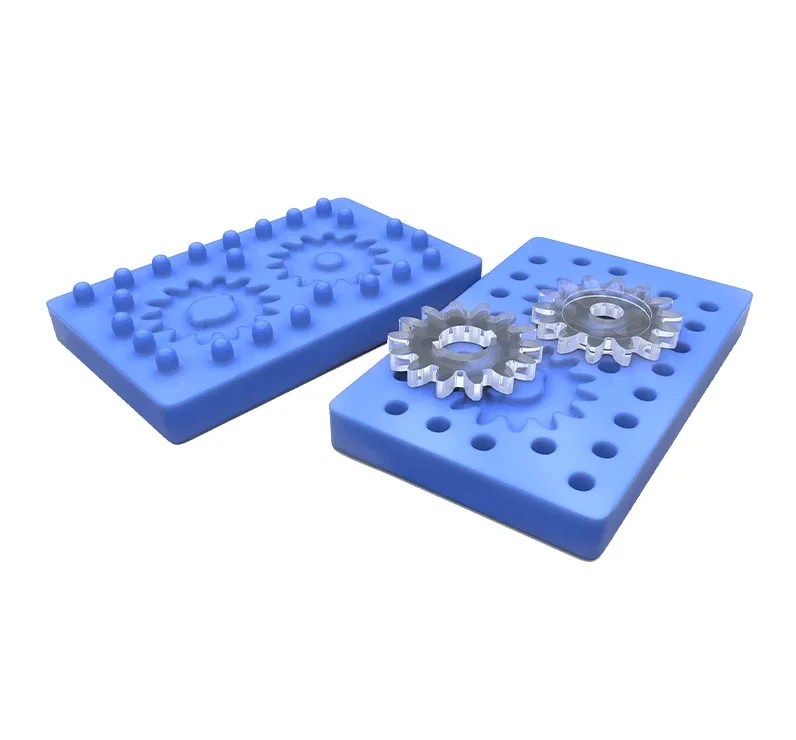 Two metal gears placed on blue silicone mold blocks with various shaped holes and protrusions, likely used for casting or manufacturing.