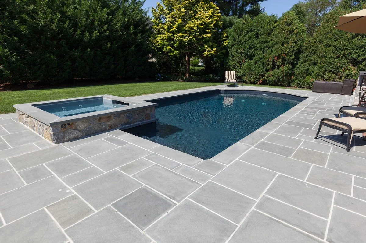 Backyard with a rectangular swimming pool, hot tub, patio furniture, and trees in the background.