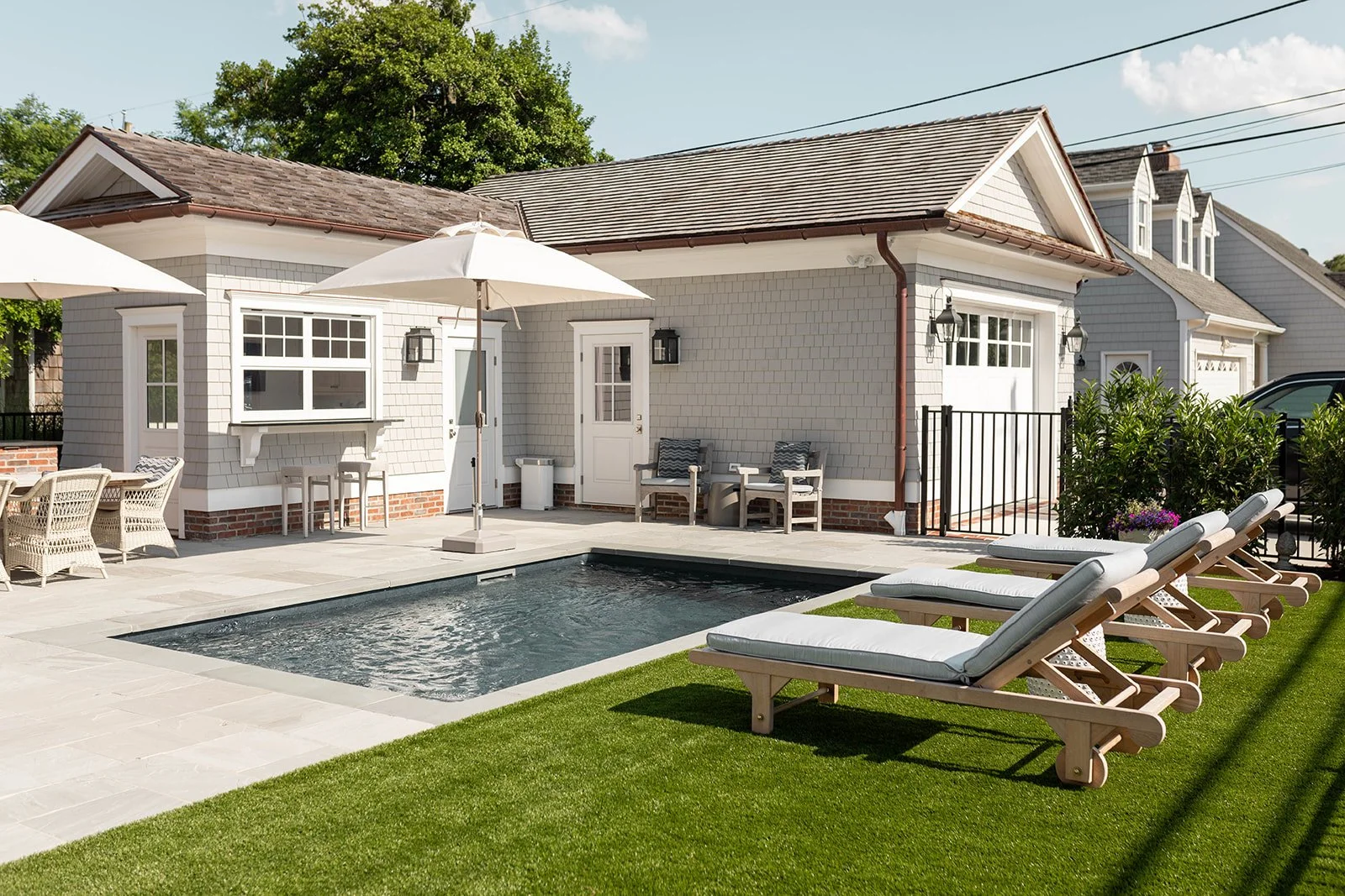 Backyard with swimming pool, lawn chairs, patio, outdoor furniture, and a small house with white siding, windows, and doors.