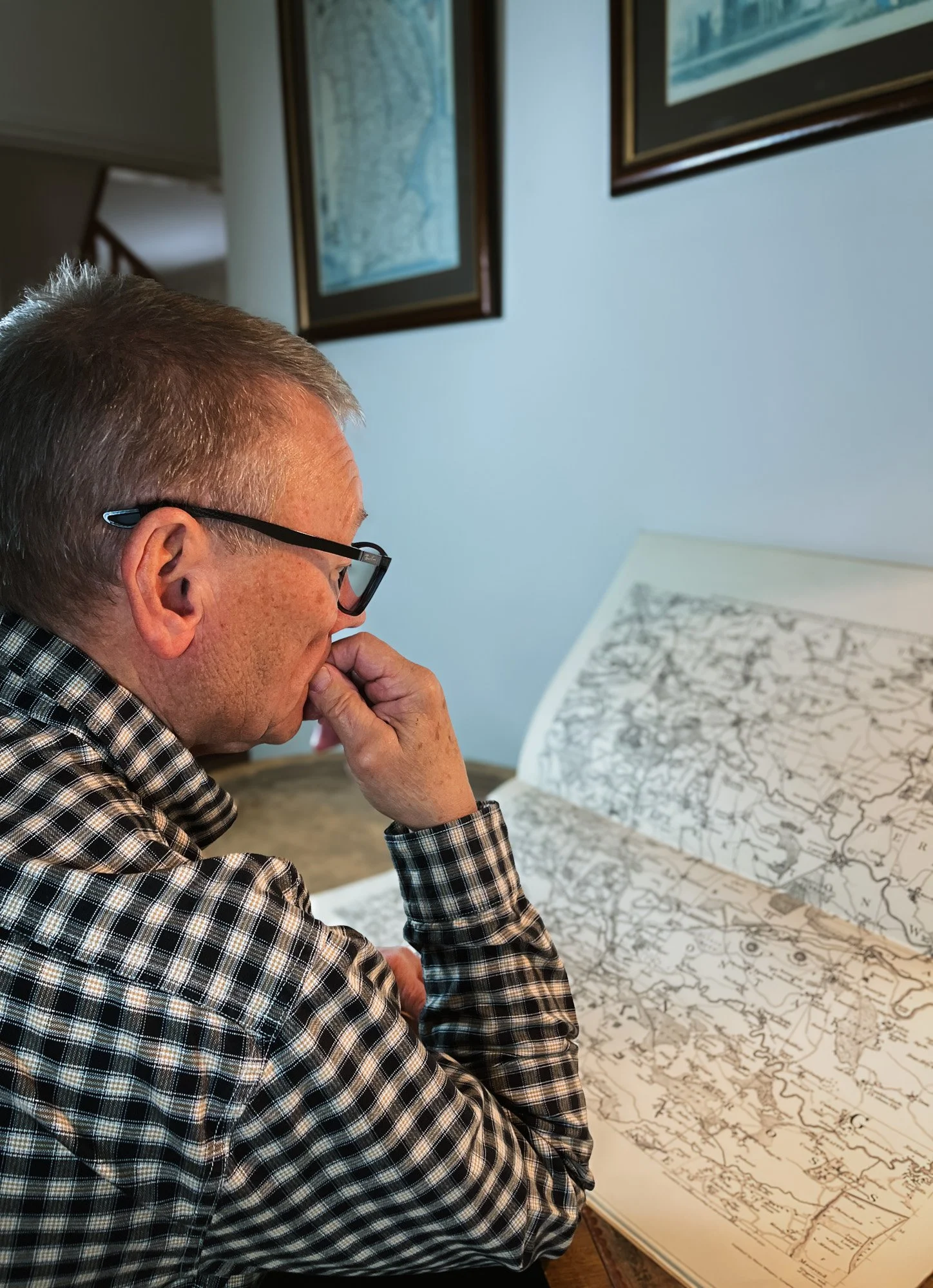 The author Alistair Hall is studying a large open map book.