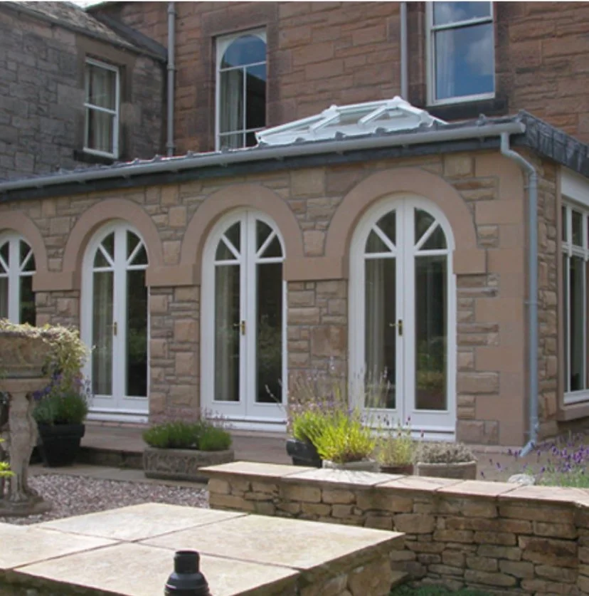 Backyard with stone patio, potted plants, and a house with arched windows and a stone exterior.
