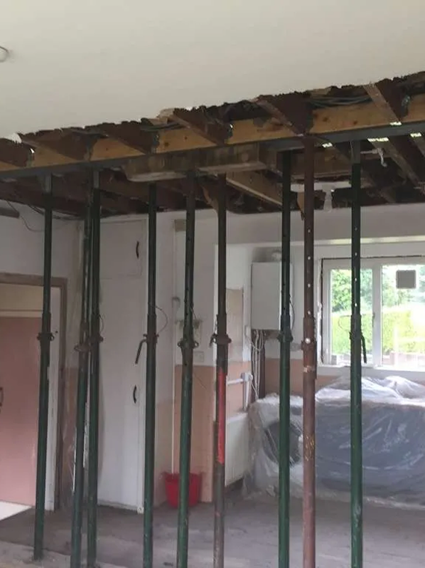 Interior of a room under renovation with exposed ceiling supports and a plastic-covered object near a window.
