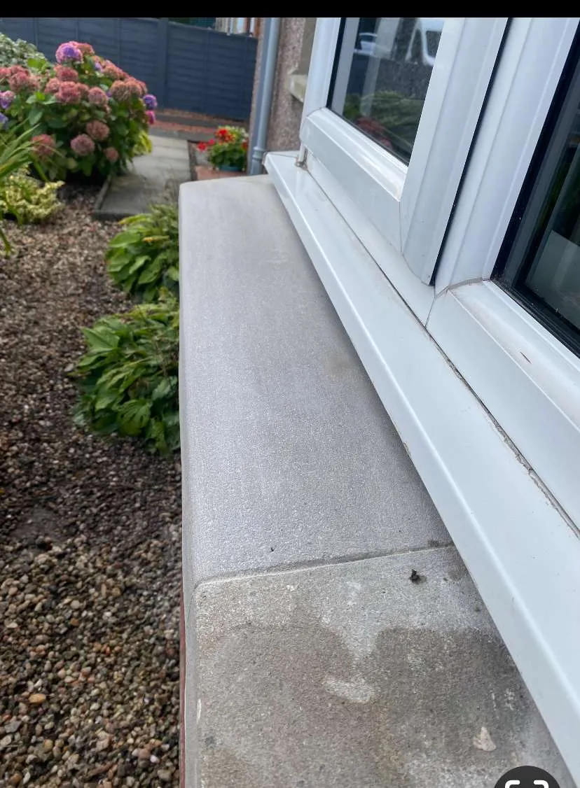 Close-up of a window sill and flower bed outside a house with blooming pink and purple hydrangea flowers.
