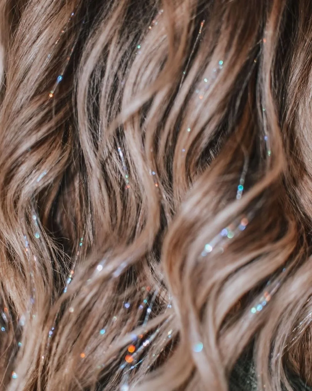 Close-up of wavy, light brown hair with embedded glitter particles.