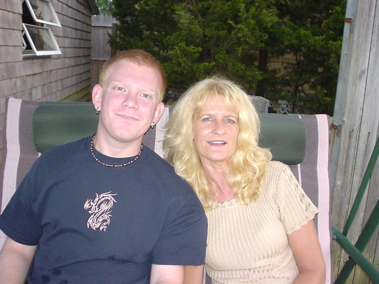 Linda Hess Lambert with son John John wearing a black t-shirt with a dragon design sitting outdoors in Cape May NJ on a patio with trees in the background.