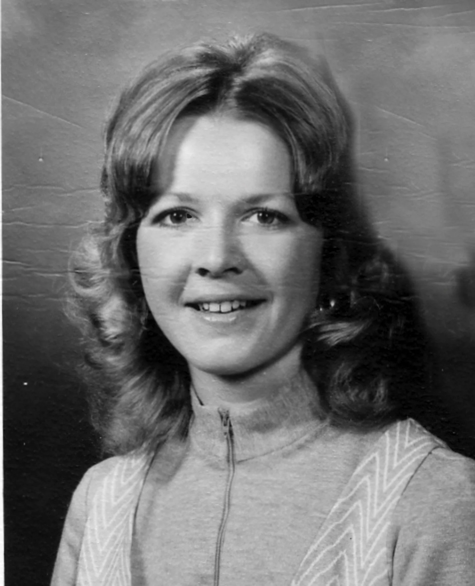 Close-up black and white photograph of Bonnie Hess-Rulli with wavy hair, smiling, wearing a light-colored top, against a plain background.
