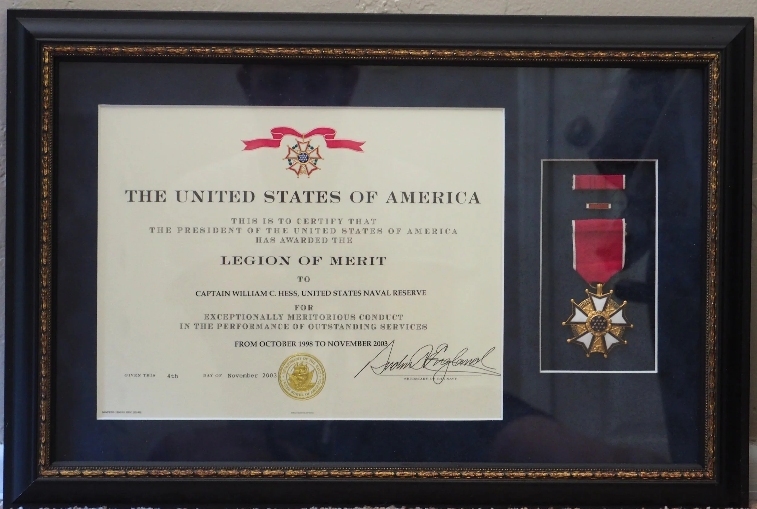 Framed medal certificate of honor from the United States of America awarded to Captain William C. Hess, next to the Legion of Merit medal signed by the Secretary of the Navy "for the President of the United States.