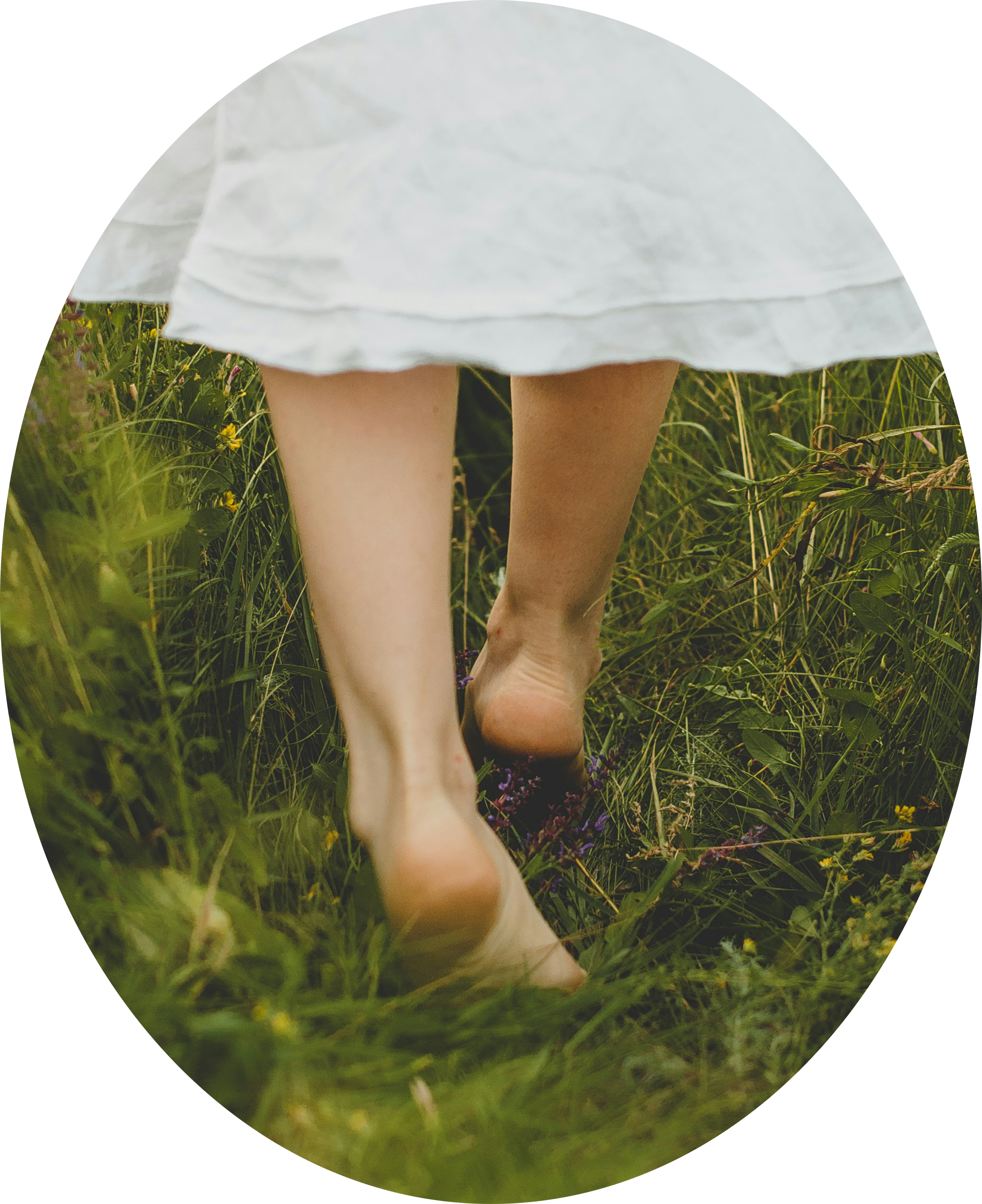 Close-up of a person's legs and feet walking through a grassy field wearing a white dress.