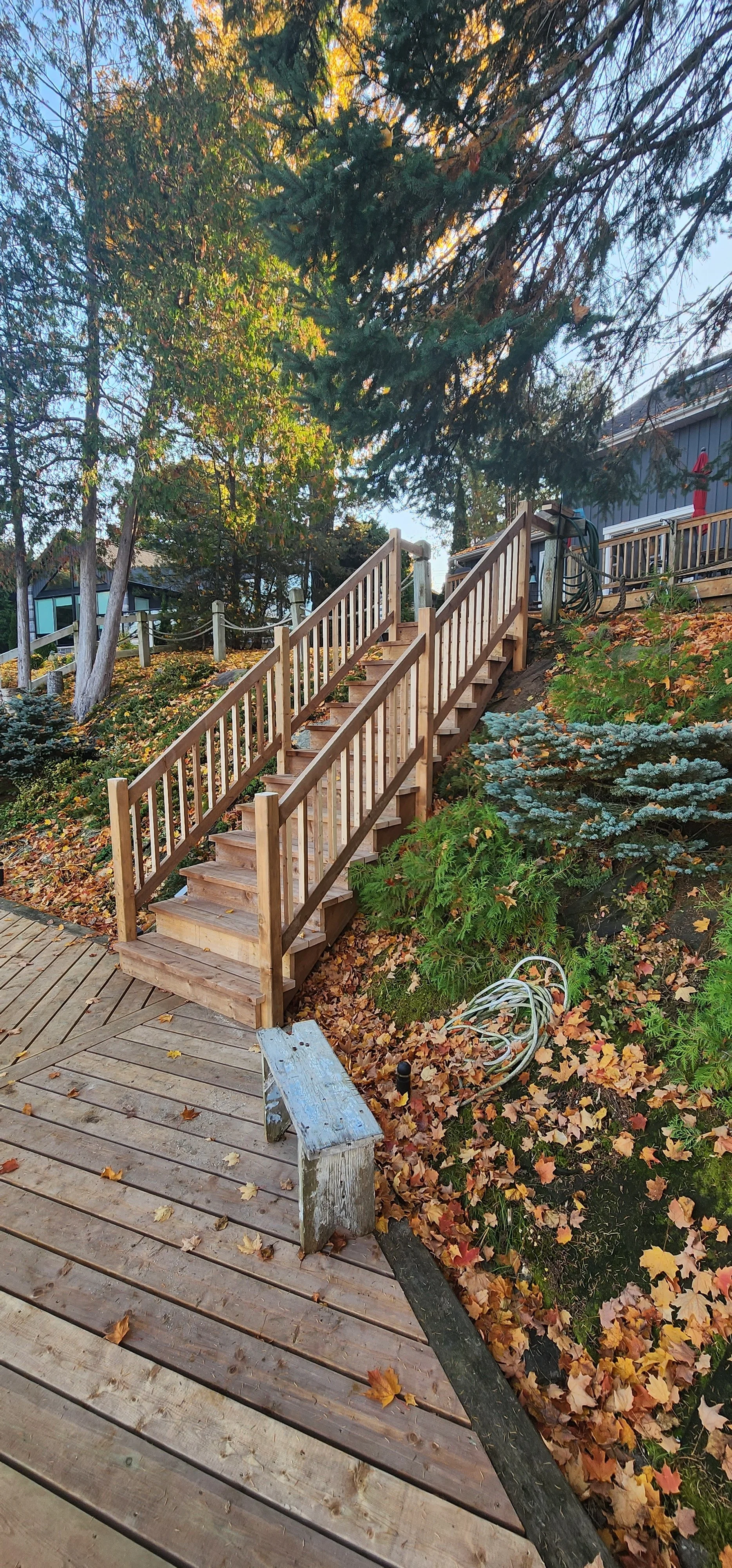 A newly built wooden staircase and deck on a hillside with autumn leaves scattered on the ground and surrounding foliage.