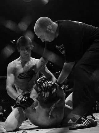 Mixed martial arts fight with a referee checking a fallen fighter in a cage