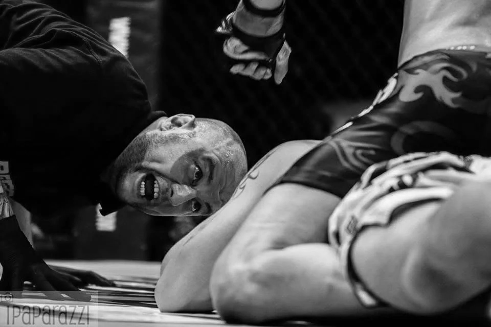 Mixed martial arts fighter on the ground after a match, smiling and celebrating with friends around him.