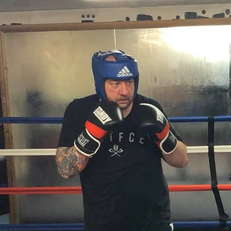 A man wearing a blue boxing headgear and black boxing gloves practicing boxing in a ring.