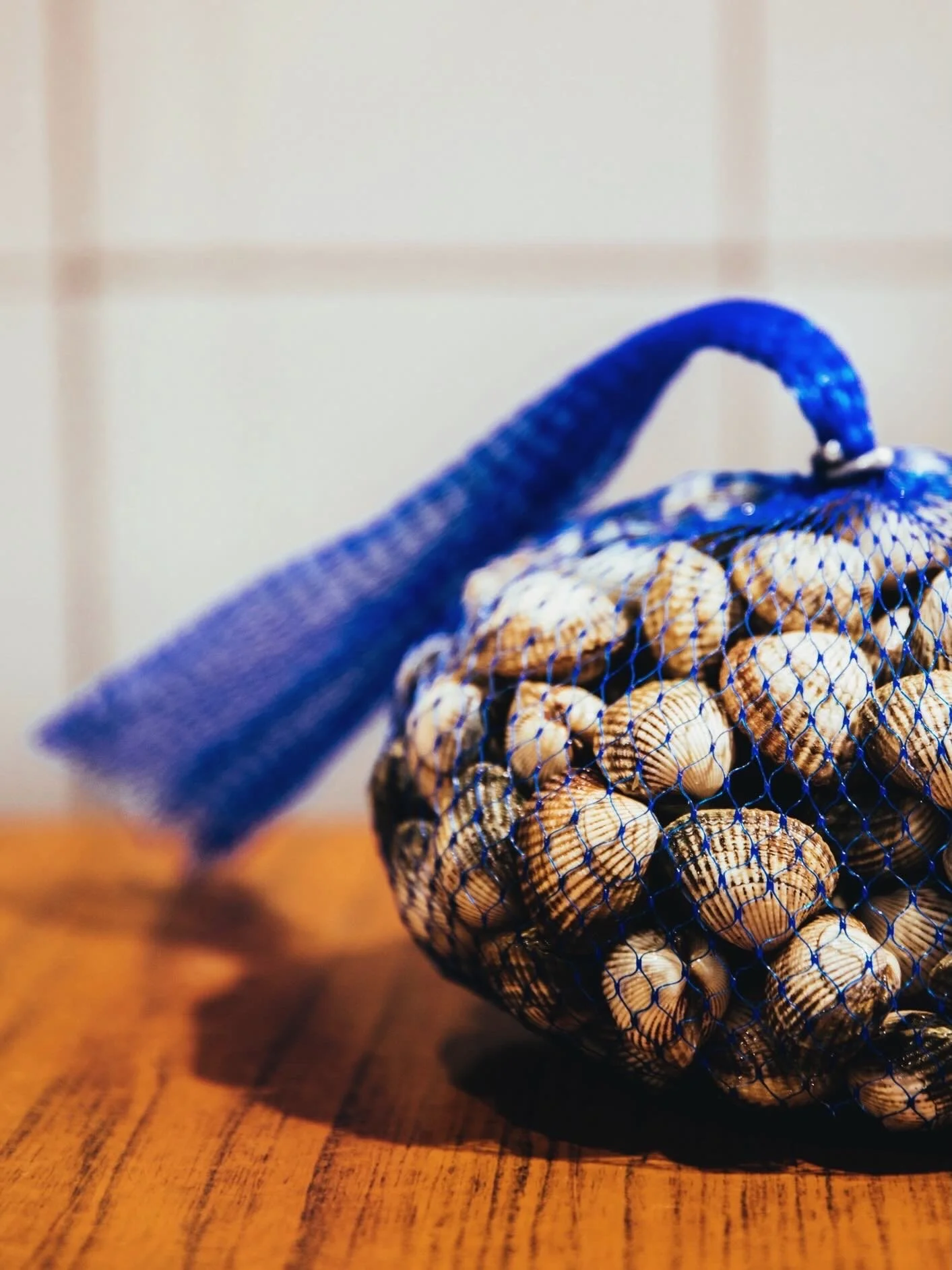 Sac en filet de snacks, rempli de coquillages, posé sur une table en bois.