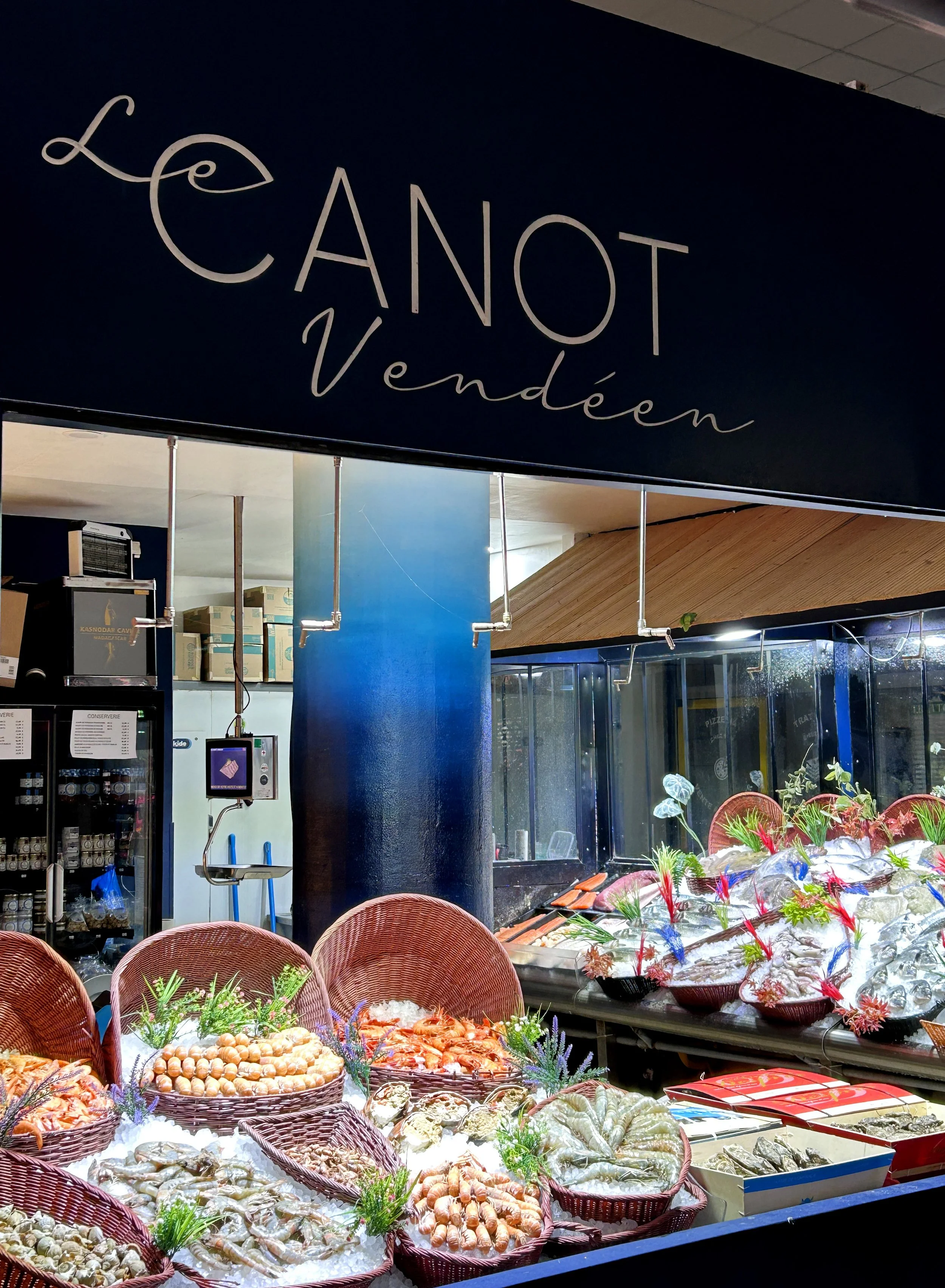 Vitrine de fruits de mer frais, avec des homards, crevettes, huîtres, et autres fruits de mer, dans une poissonnerie ou marché, décorée avec des plantes et des aliments sur glace.