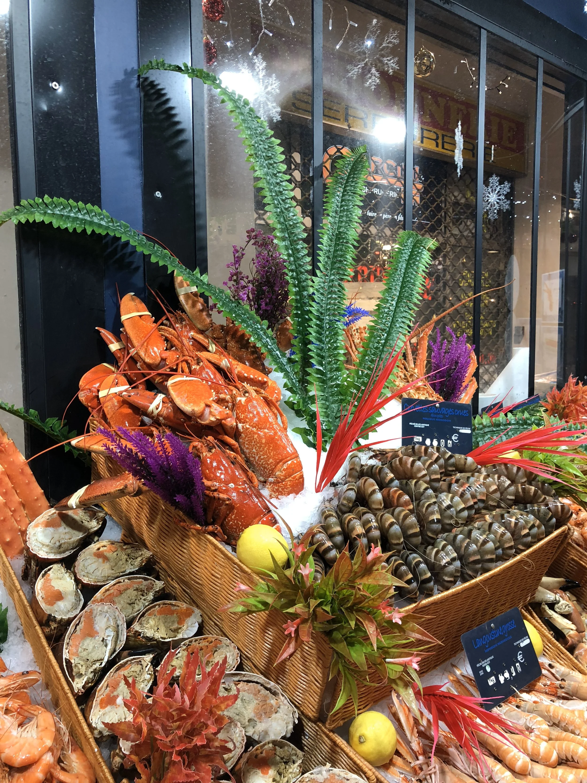 Étagère avec des homards, des huîtres, des coquillages, des végétaux en plastique, et des décorations de Noël en arrière-plan dans un magasin de produits de la mer.