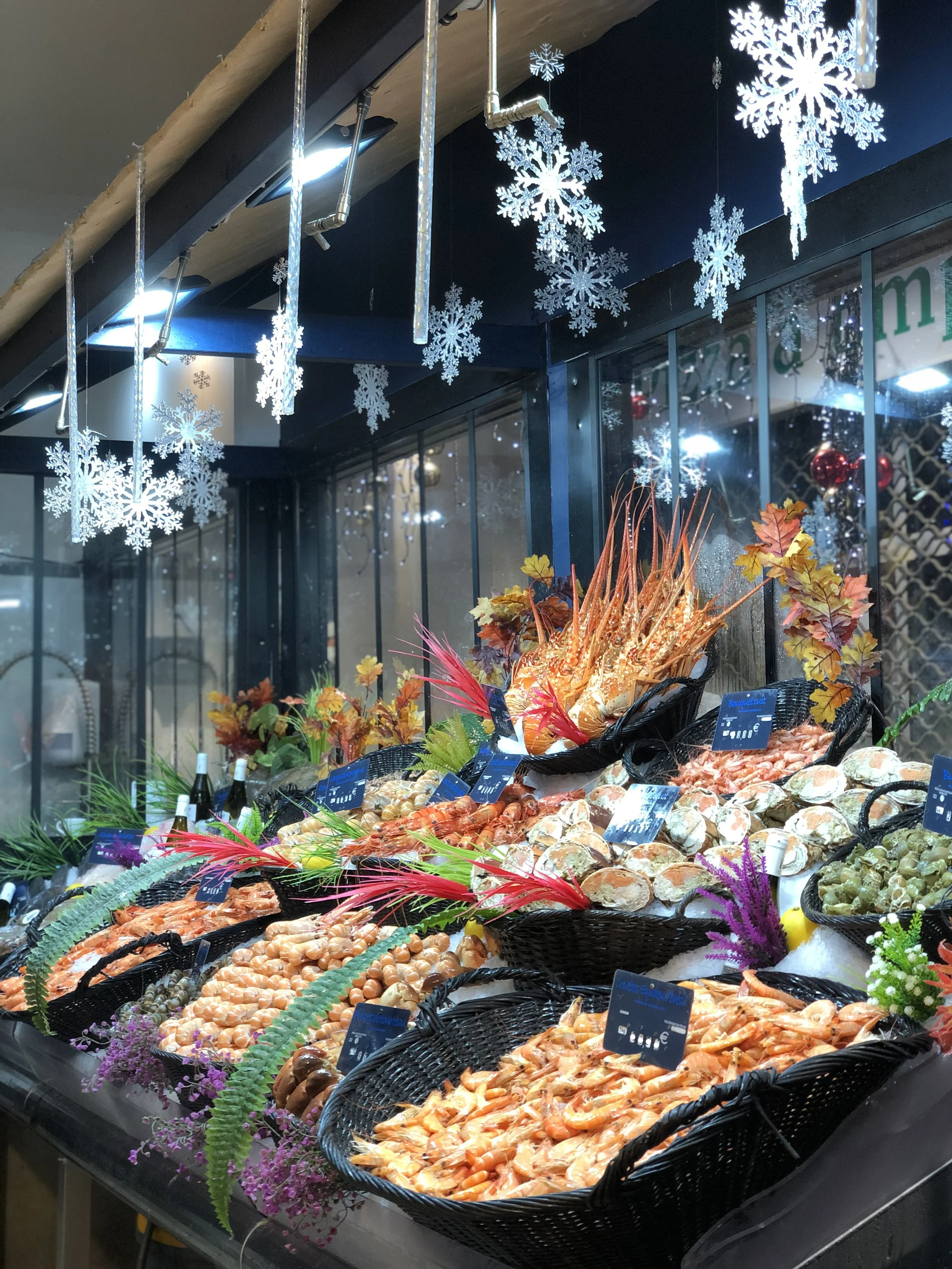 Marché de fruits de mer avec coquillages, crevettes et autres crustacés, décoré avec des éléments de décoration automnale et des flocons de neige suspendus.